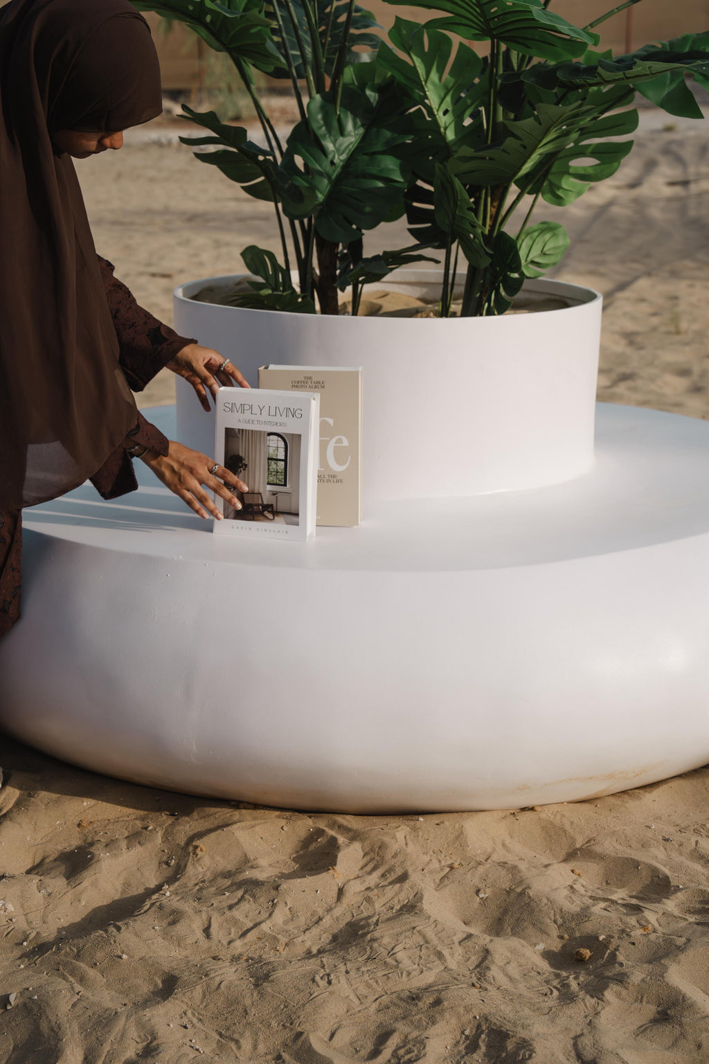 Person interacting with a book on a white donut shaped planter seater