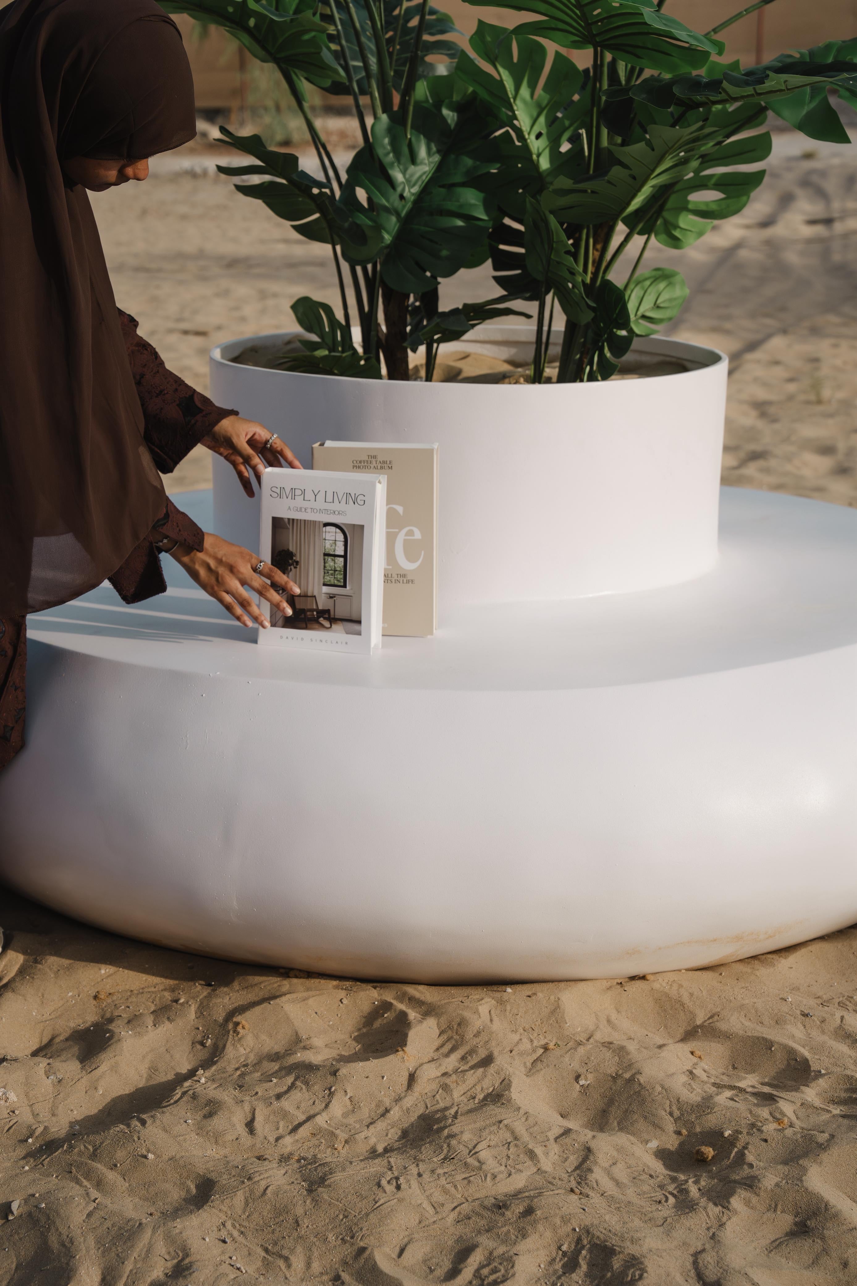Person interacting with a book on a white donut shaped planter seater